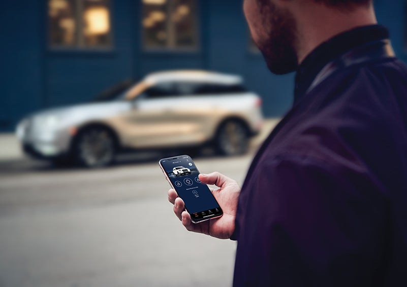A person is shown interacting with a smartphone to connect to a Lincoln vehicle across the street. | Sheehy Lincoln of Richmond in Richmond VA